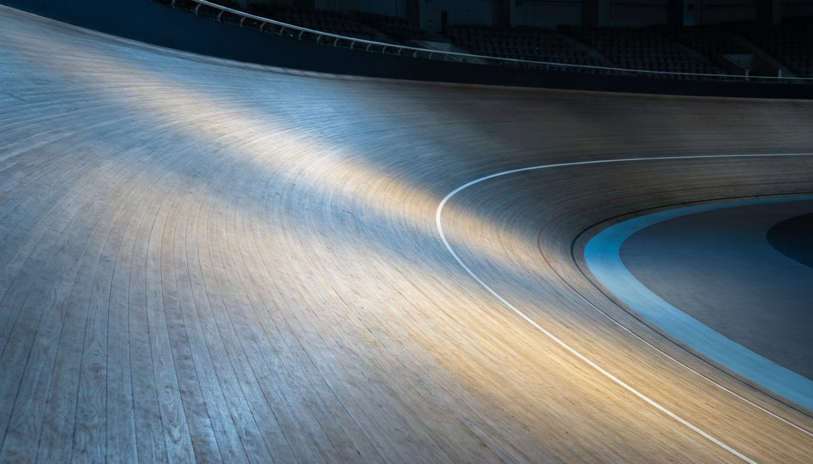AI生成示意图:室内自行车馆的木质倾斜赛道与白色标线,灯光下的空看台